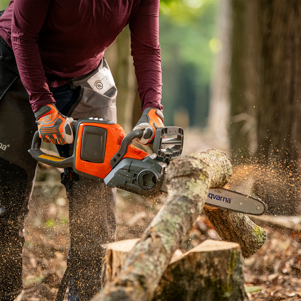 Eine Person sägt mit einer Kettensäge einen Baumstamm. Husqvarna Logo sichtbar.