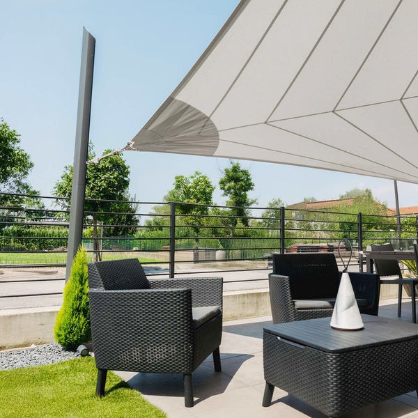 Moderne Terrasse mit hellgrauem Sonnensegel an dunklem Metallpfosten, schwarzen Polyrattan-Sesseln und passendem Tisch auf hellem Fliesenboden.