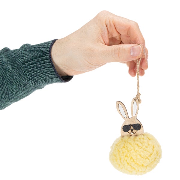 Eine Hand hält einen Osteranhänger mit einem hölzernen Hasenkopf mit Sonnenbrille und einem gelben Bommel.