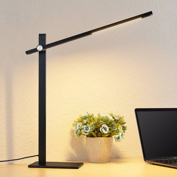 Moderne schwarze LED-Schreibtischleuchte mit verstellbarem Arm auf einem Arbeitstisch neben Blumen und Laptop.
