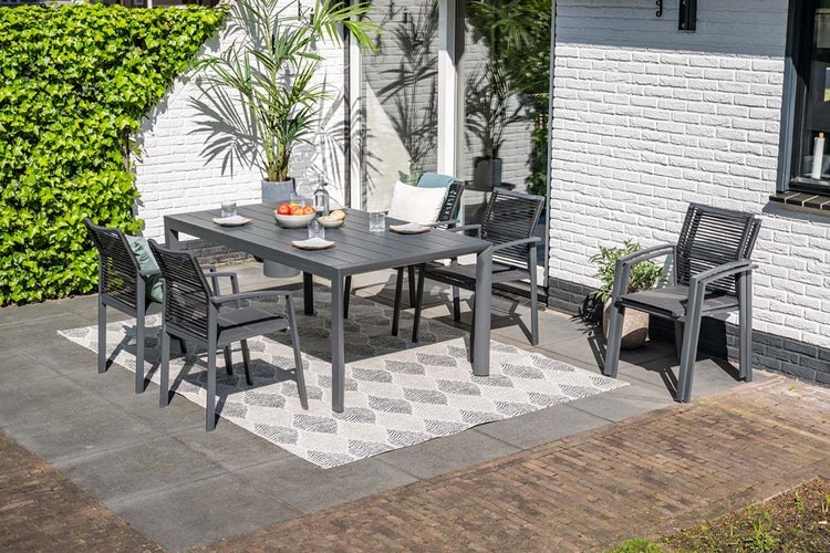Modernes Gartenmöbel-Set aus grauem Aluminium mit rechteckigem Tisch und fünf Stühlen auf einer gepflasterten Terrasse mit Außen-Teppich.