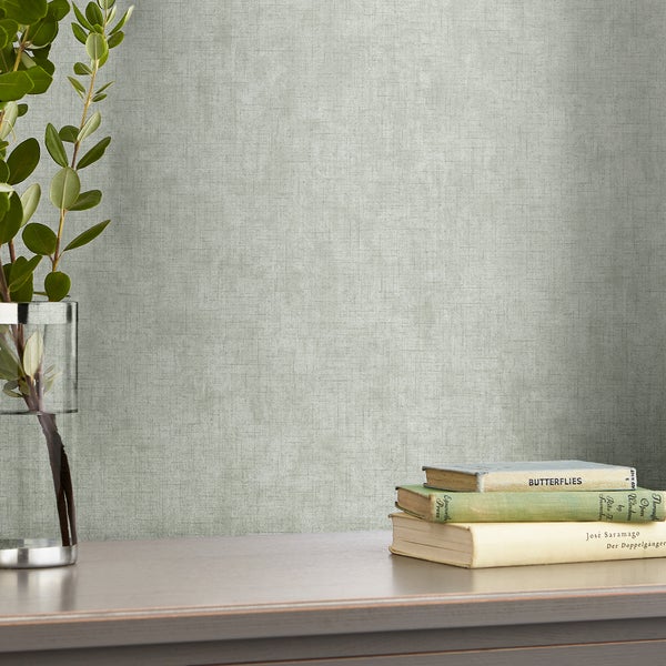 Vlies-Tapete mit dezenter Textilstruktur vor Wand mit Zimmerpflanze in Glasvase und Bücherstapel auf einem Tisch