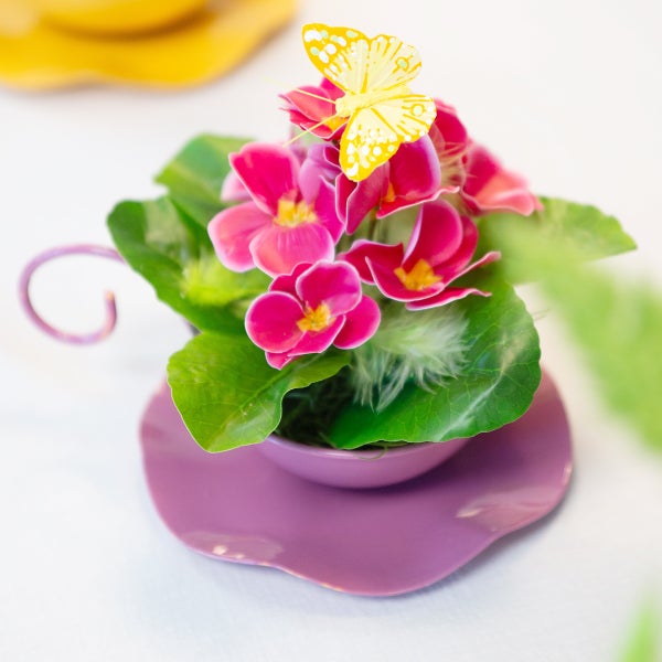 Dekorative Tischdekoration mit Primelblüten, Blättern und einem Schmetterling in einer Tasse.