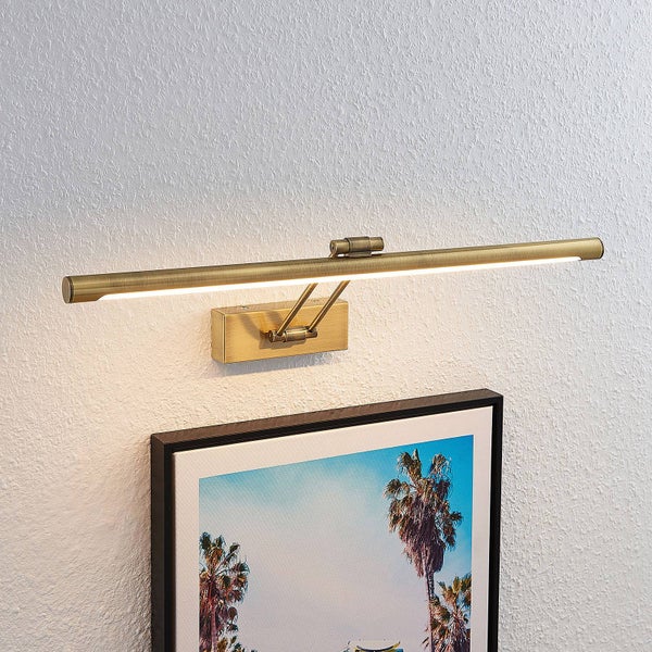 LED-Bilderleuchte aus Messing antik über einem gerahmten Bild an einer weiß strukturierten Wand.