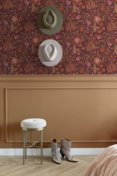Organisierter Raum mit floral gemusterter Tapete, Wandpaneelen, einem runden Hocker mit Metallgestell, Hüten und Stiefeln.