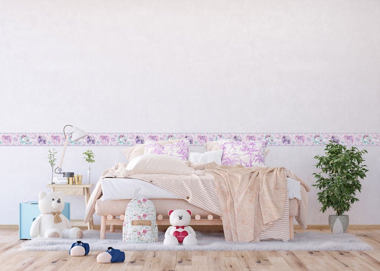 Hell gestaltetes Kinderzimmer mit einer horizontalen selbstklebenden Bordüre mit Einhorn-Motiv an einer weißen Wand über einem Bett.