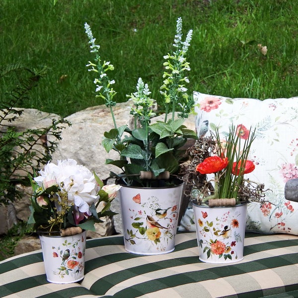 Dekorative Szene mit drei bepflanzten Töpfen mit Vogelmotiven und einem Blumenkissen auf einer Bank