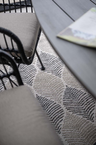 Flachgewebter Outdoor-Teppich mit Blattmuster unter Gartentisch und Stühlen.