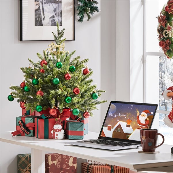 Weihnachtlich dekorierter Schreibtisch mit kleinem Weihnachtsbaum, Geschenken, Laptop und Tasse.