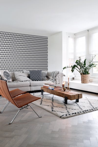 Heller Wohnraum mit Sofa, Holztisch, Teppich und geometrischer Tapete.