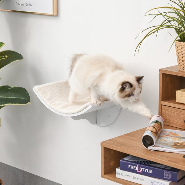 Moderne Wand-Katzenliege mit Plüscheinlage. Eine flauschige Katze steigt von der Ablage auf ein Holzregal in einer hellen, organisierten Umgebung.