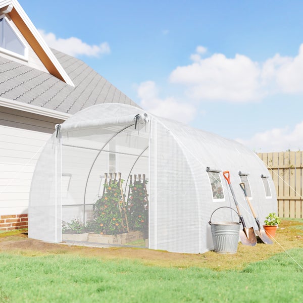 Weißes Folien-Gewächshaus im Garten mit aufgerolltem Eingang, Tomatenpflanzen im Inneren, Eimer und Spaten davor auf einer Rasenfläche.