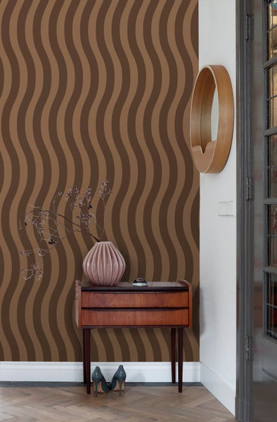 Wohnraum mit Tapete mit vertikalen Wellenstreifen in Brauntönen. Ein Sideboard aus Holz und ein runder Spiegel ergänzen das Interieur im Retro-Stil.