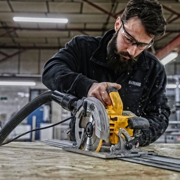 Ein Mann mit Schutzbrille benutzt eine DeWalt Tauchsäge zum Schneiden von Holz.