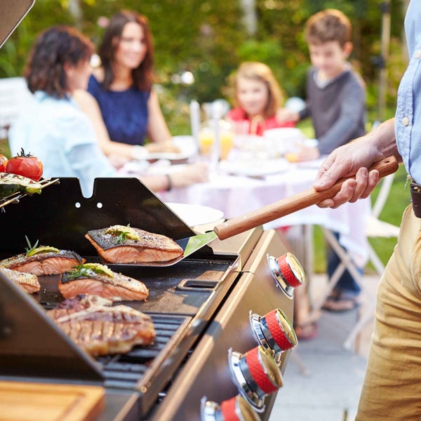 Grillszene im Freien mit Familie und Grillmeister, der Lachs und Steak auf einem Grill zubereitet
