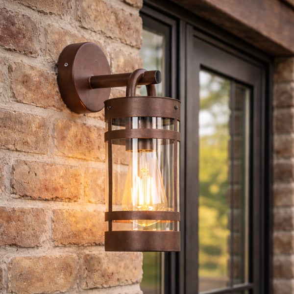 Rustikale Außenwandleuchte im Laternen-Stil aus Metall und Glas an einer Backsteinmauer.