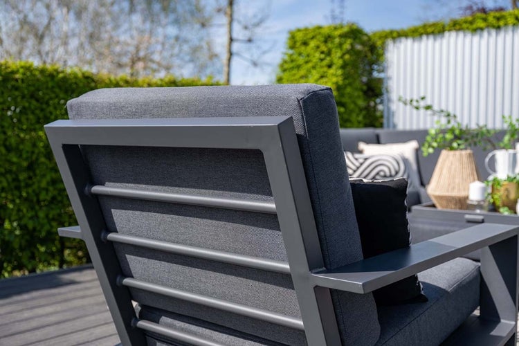 Rückansicht eines Garten-Lounge-Sessels mit dunkelgrauem Metallrahmen, horizontalen Streben und grauen Stoffpolstern auf einer Terrasse.