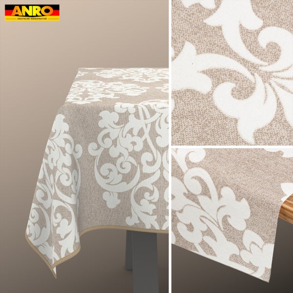 Tischdecke mit Damast-Blumenmuster aus strukturiertem Stoff, über eine Tischkante fallend. ANRO Deutsche Manufaktur Logo.
