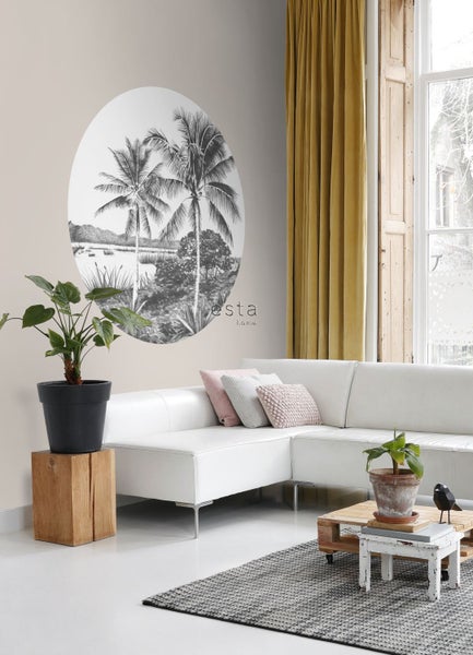 Wohnzimmer mit weißem Sofa, Zimmerpflanzen und einer Wanddekoration mit Palmenmotiv.