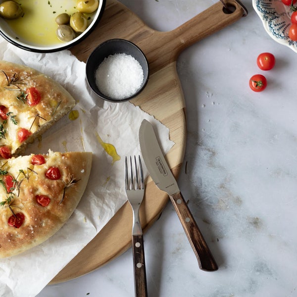 Stillleben mit Focaccia, Oliven, Salz, Gabel und Messer auf einem Schneidebrett