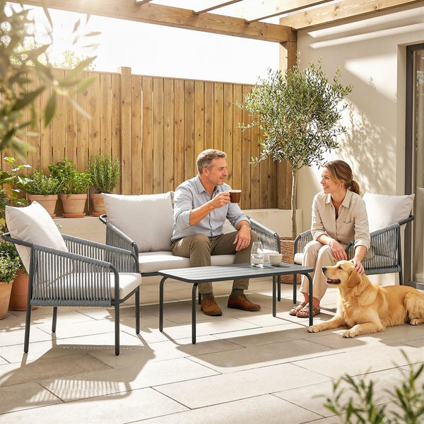 Helle Terrasse mit Garten-Lounge-Set aus Metall und Seilgeflecht, bestehend aus Sofa, Sesseln und Kaffeetisch, vor einem Holzzaun.