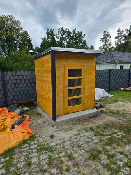 Modernes Gartenhaus aus Holz mit Pultdach, Glastür und dunklen Eckprofilen auf einem Betonfundament im Außenbereich.