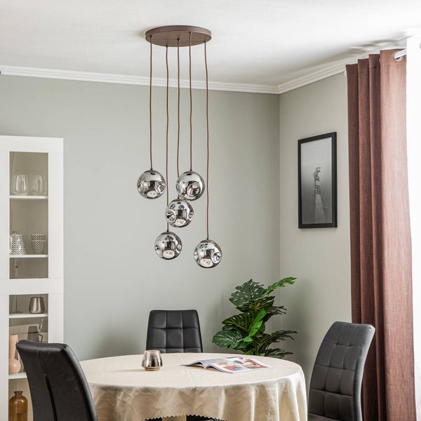 Moderne 5-flammige Pendelleuchte mit Glaskugeln über einem runden Esstisch in einem hellen Raum mit schwarzen Stühlen und einer Pflanze.