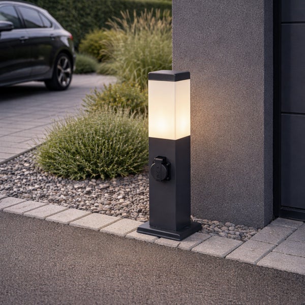 Moderne Außenstandleuchte in Anthrazit mit integrierter Steckdose und warmweißem Licht in einer Garageneinfahrt.