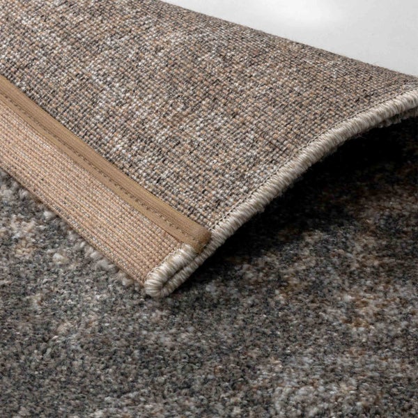 Detailaufnahme eines Teppichs mit Fokus auf die gewebte Struktur der Rückseite und den umnähten Rand.