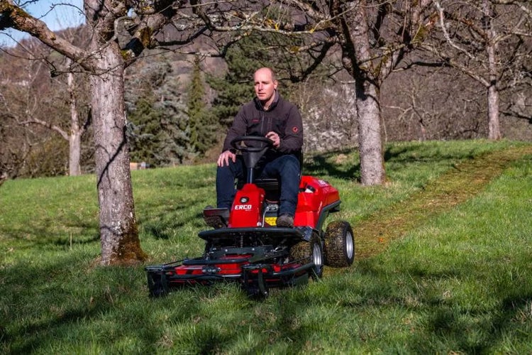 Ein Mann bedient einen roten Erco Aufsitzmäher auf einer grünen Wiese mit Bäumen.