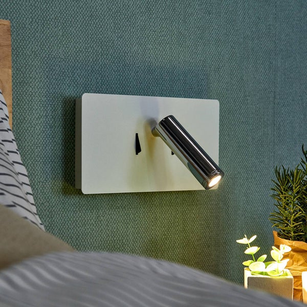 Moderne Wand-Leseleuchte mit weißer rechteckiger Basis und schwenkbarem Chrom-Spot an einer grünen strukturierten Wand.