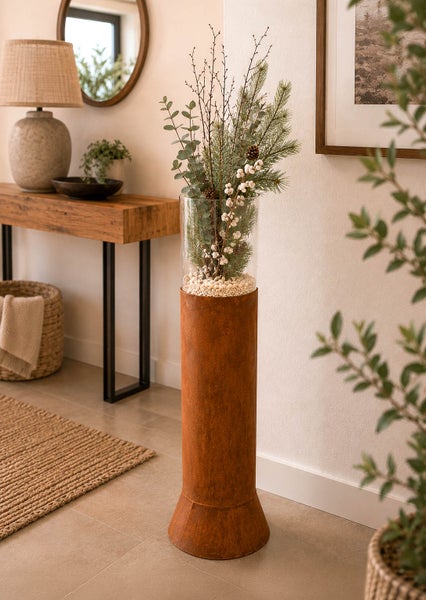 Hohe Standvase mit Rostoptik und Glasaufsatz, dekoriert mit Zweigen in einem modernen Wohnraum.