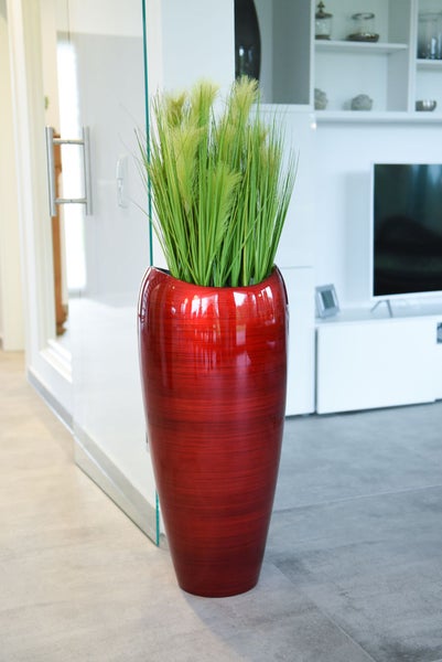 Helles, modernes Wohnzimmer mit weißem TV-Möbel, einer Glastür und einer großen, glänzenden roten Bodenvase mit künstlichem Gras.