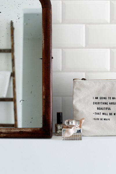 Badezimmerszene mit Spiegel, Kosmetiktasche und Kosmetikprodukten auf einem weißen Regal