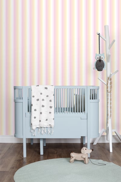 Babyzimmer mit blauem Gitterbett, weißer Decke, rundem Teppich und Holzspielzeug