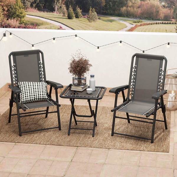 Balkonset mit zwei grauen Klappstühlen, einem schwarzen Beistelltisch und einem Outdoorteppich auf einer Terrasse mit Lichterkette.