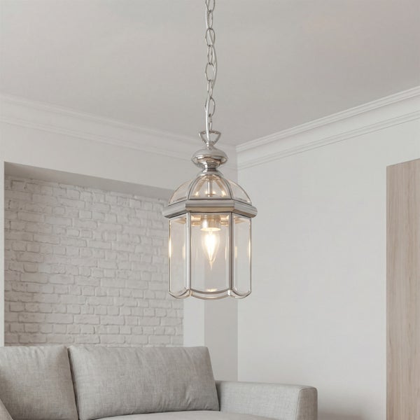 Hängeleuchte im Laternendesign mit verchromtem Metallrahmen und klaren Glaspaneelen in einem hellen Wohnzimmer über einem Sofa.