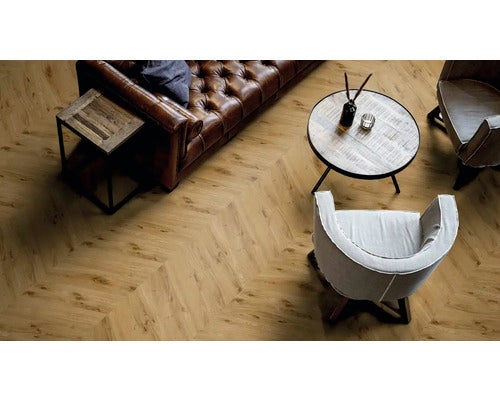 Bodenbelag mit Chevron-Muster in Holzoptik in einem Wohnzimmer mit Ledersofa und Holztischen.