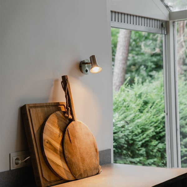 Moderne Wandleuchte aus Metall in einer hellen Küche. Die Spotleuchte beleuchtet Holz-Schneidebretter auf der Arbeitsplatte neben dem Fenster.