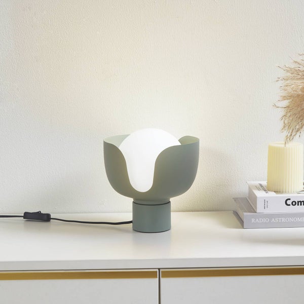 Moderne Tischleuchte mit weißer Glaskugel in einer tulpenförmigen graugrünen Halterung auf einem weißen Möbelstück.