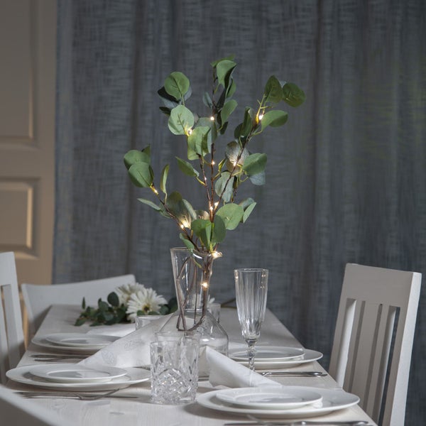 Dekorierter Esstisch mit Eukalyptusstrauß in einer Vase und Lichterkette