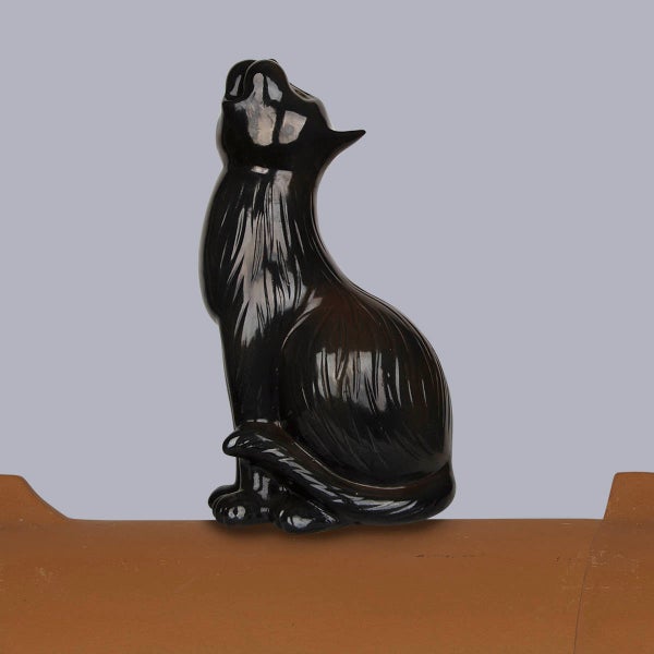 Dachfigur Katze in Schwarz aus glasierter Keramik, sitzend und aufblickend, montiert auf einem Firstziegel.