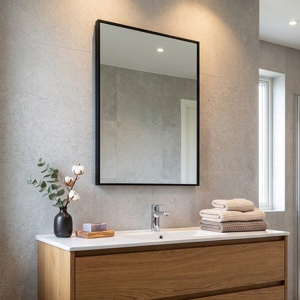 Modernes Badezimmer mit rechteckigem Spiegel mit schwarzem Rahmen, weißem Waschtisch auf Holzunterschrank und grauen Wandfliesen in Steinoptik.