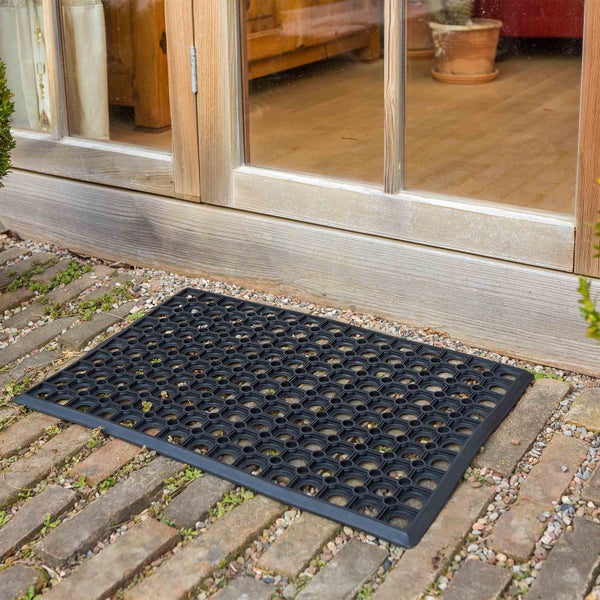 Schwarze Gummifußmatte vor einer Holztür auf einem Steinweg