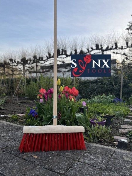 Rote Kehrbürste mit Holzstiel im Garten