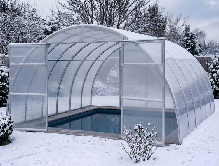 Poolüberdachung mit gewölbter Form und transparenten Paneelen in verschneiter Gartenlandschaft.