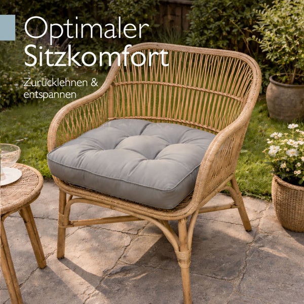 Gartenstuhl aus Rattan mit weichem Sitzpolster auf einer Terrasse stehend.