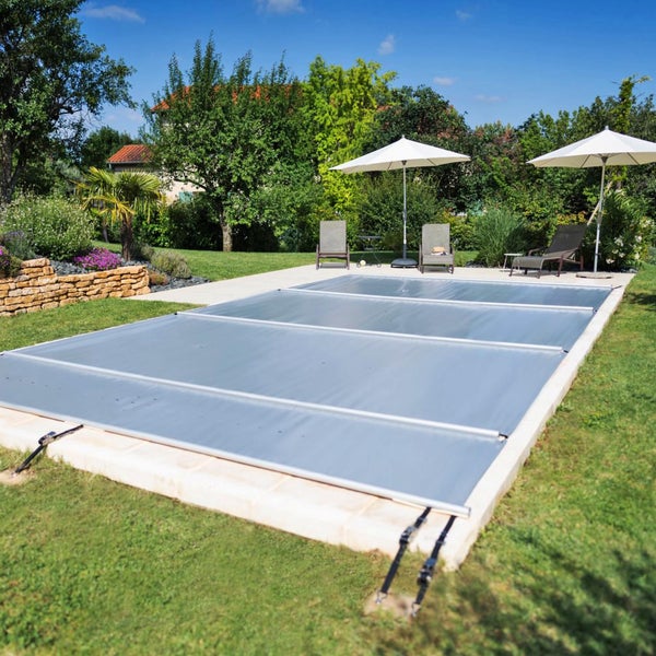 Abgedecktes Schwimmbecken mit Poolabdeckung im Garten mit Liegestühlen und Sonnenschirmen