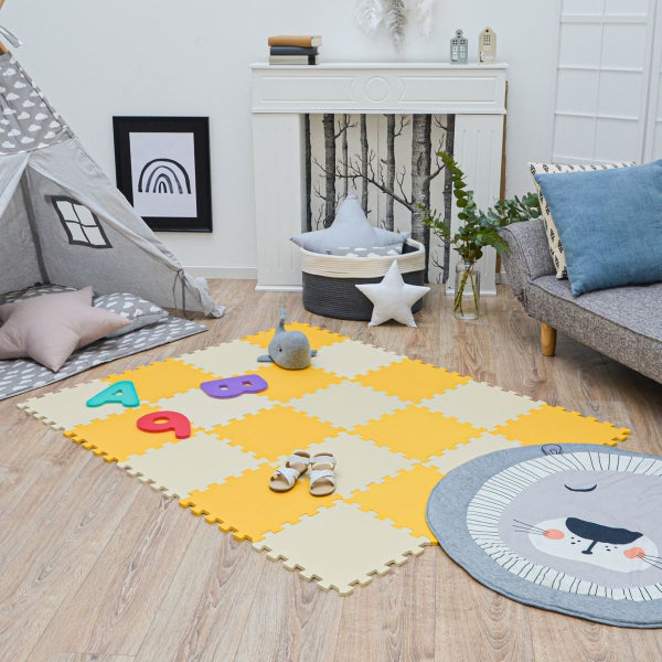 Hell eingerichtetes Kinderzimmer mit gelb-beiger Puzzlematte aus Schaumstoff, einem grauen Tipi-Zelt und einem runden Löwen-Teppich auf Holzboden.