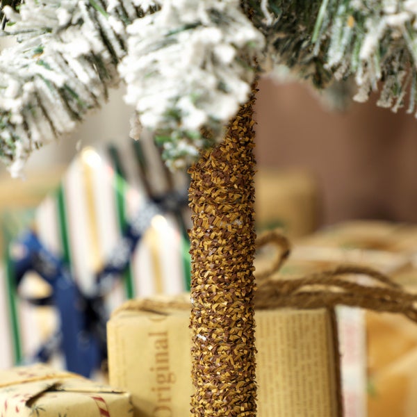 Nahaufnahme eines künstlichen Weihnachtsbaums mit schneebedeckten Zweigen und strukturiertem braunem Stamm vor Geschenken.